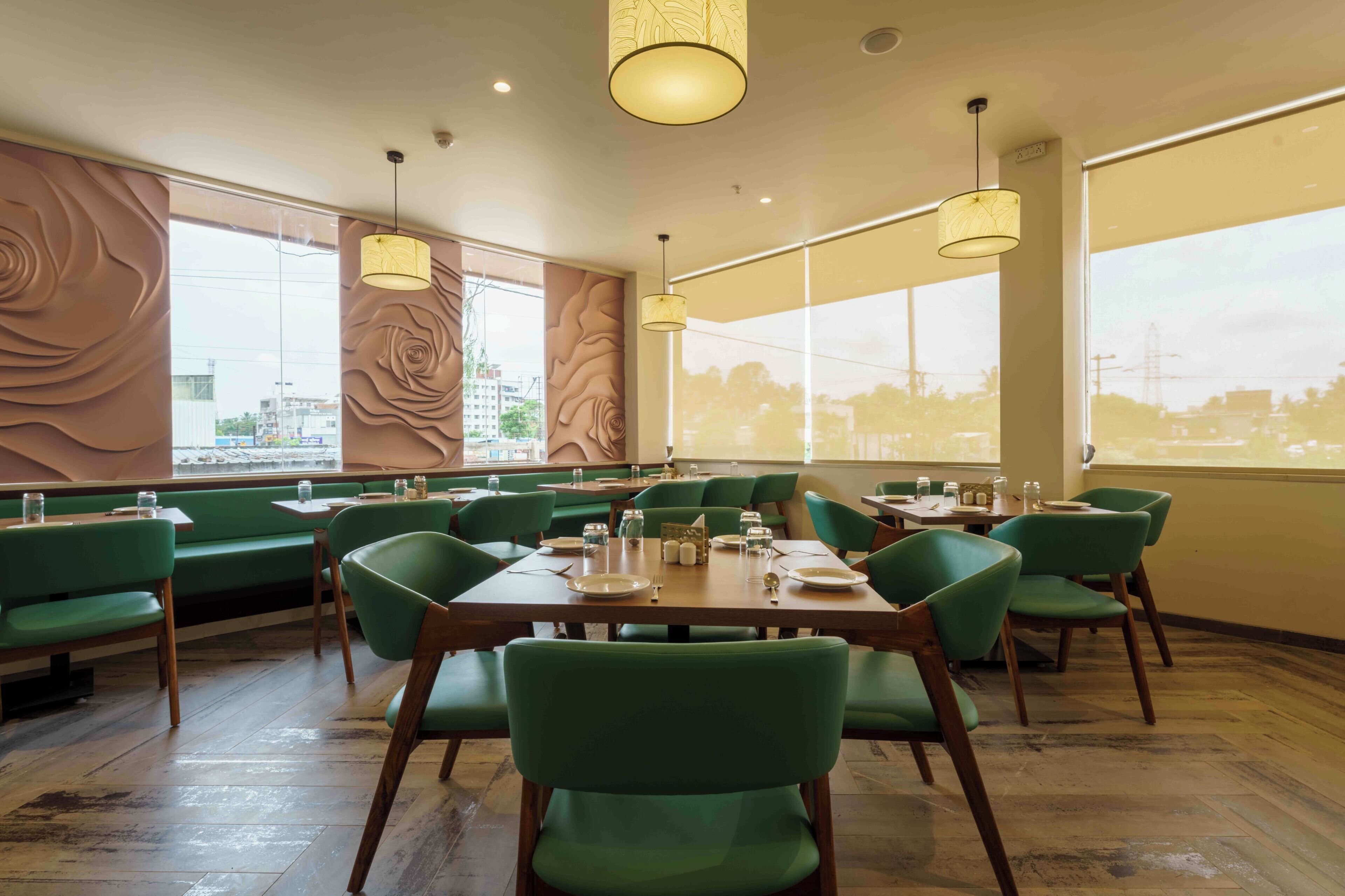 Ein Restaurant mit grün gepolsterten Sitzecken und Tischen, großen Fenstern mit Stadtblick und Pendelleuchten.