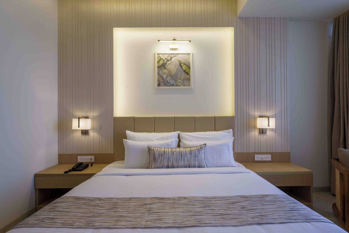 Une chambre d’hôtel avec un grand lit, deux tables de chevet, une petite table, un téléphone et des lampes fixées au mur.