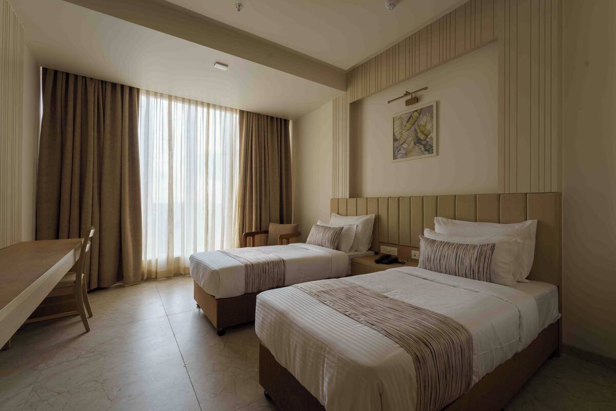 Une chambre d’hôtel avec deux lits, un bureau et une fenêtre avec des rideaux.