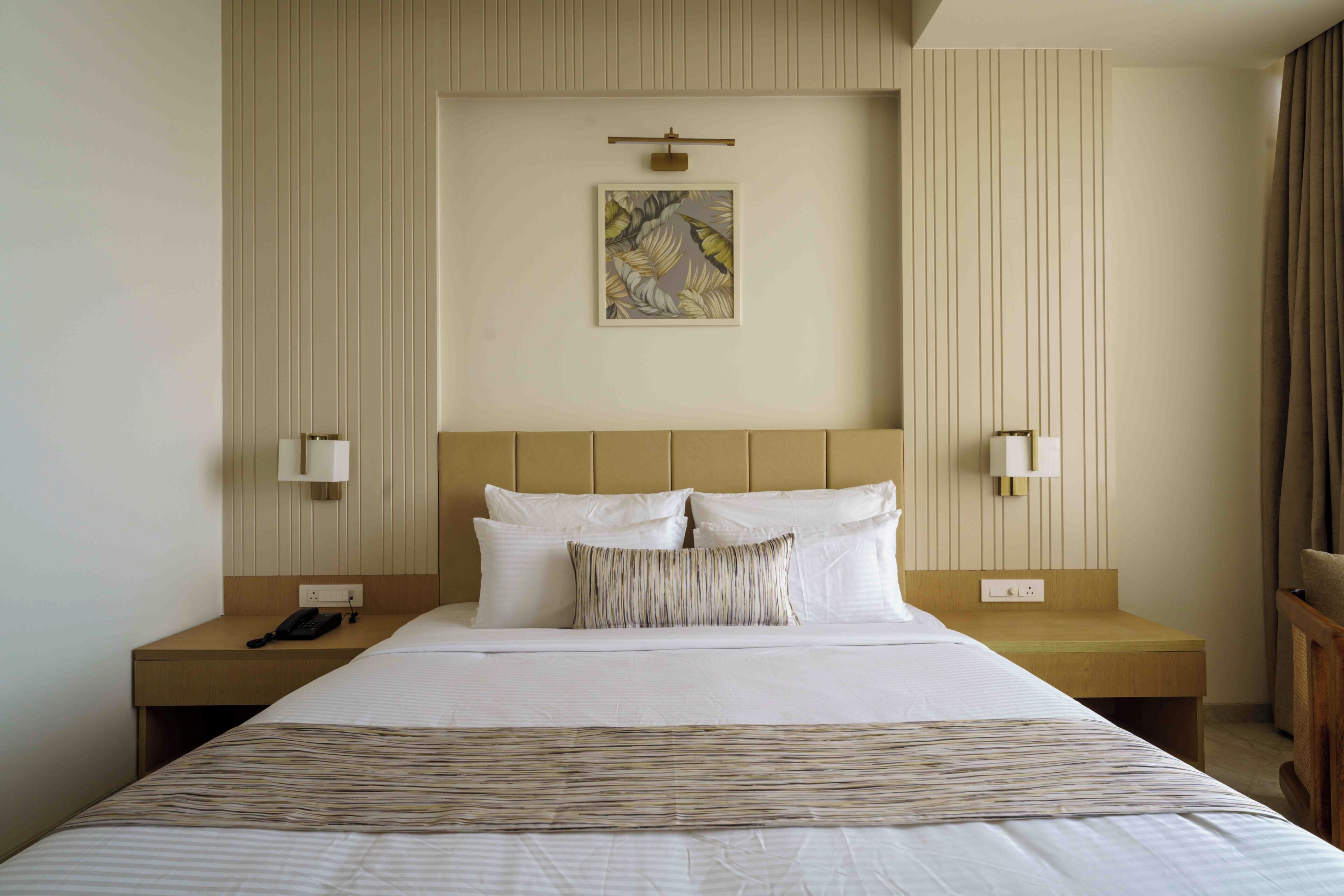 A hotel room with a bed, two bedside tables, a telephone, a wall-mounted light, and a painting.