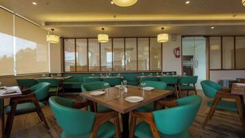 A restaurant with booths and tables, wooden flooring, and hanging pendant lights.