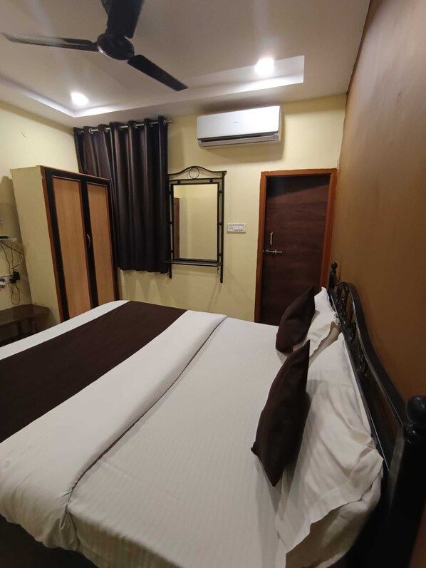 Une chambre à coucher comprenant un lit, un ventilateur de plafond, un appareil de climatisation, une armoire, un miroir et une porte.
