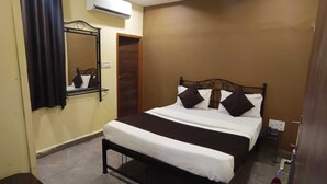 Un dormitorio con cama, ventilador de techo, equipo de aire acondicionado, una mesita y un espejo.