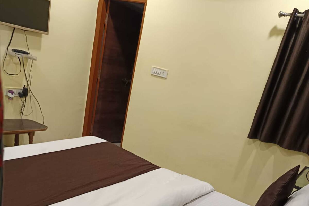 Una camera d'albergo con un letto, una televisione fissata al muro, una porta e una presa di corrente.