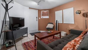 A living room with a sofa, a coffee table, a TV on a stand, a lamp, and artwork on the wall. - 3br with Private Entrance - Garden Unit (Chicago)