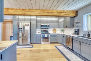 A modern kitchen with stainless steel appliances, grey cabinetry, and a wooden ceiling.