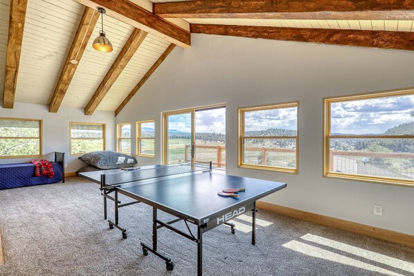 Una mesa de ping pong en una habitación con ventanas amplias y techo inclinado.