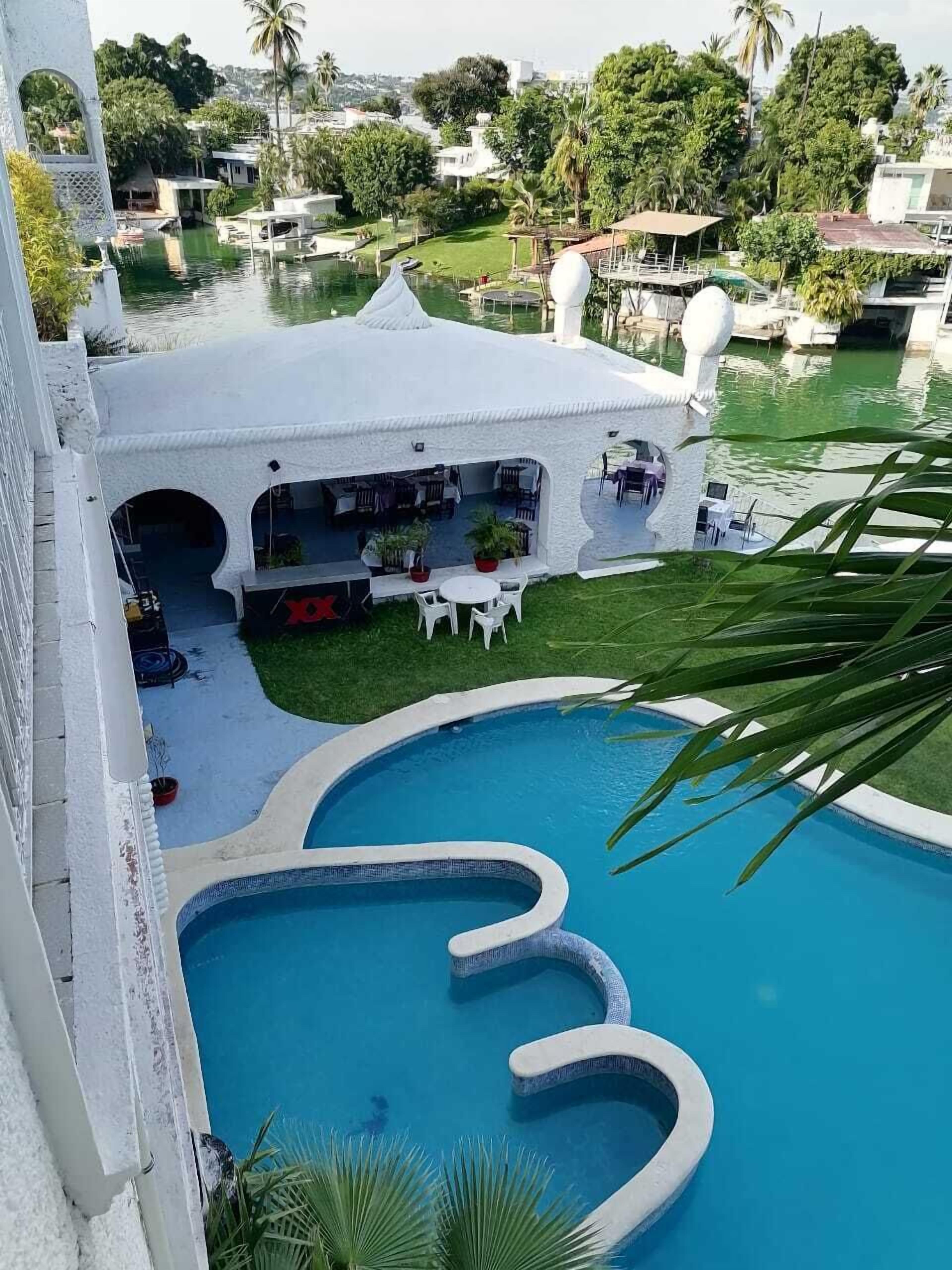 A pool with a unique design, a covered outdoor seating area, and a view of the surrounding greenery and buildings.