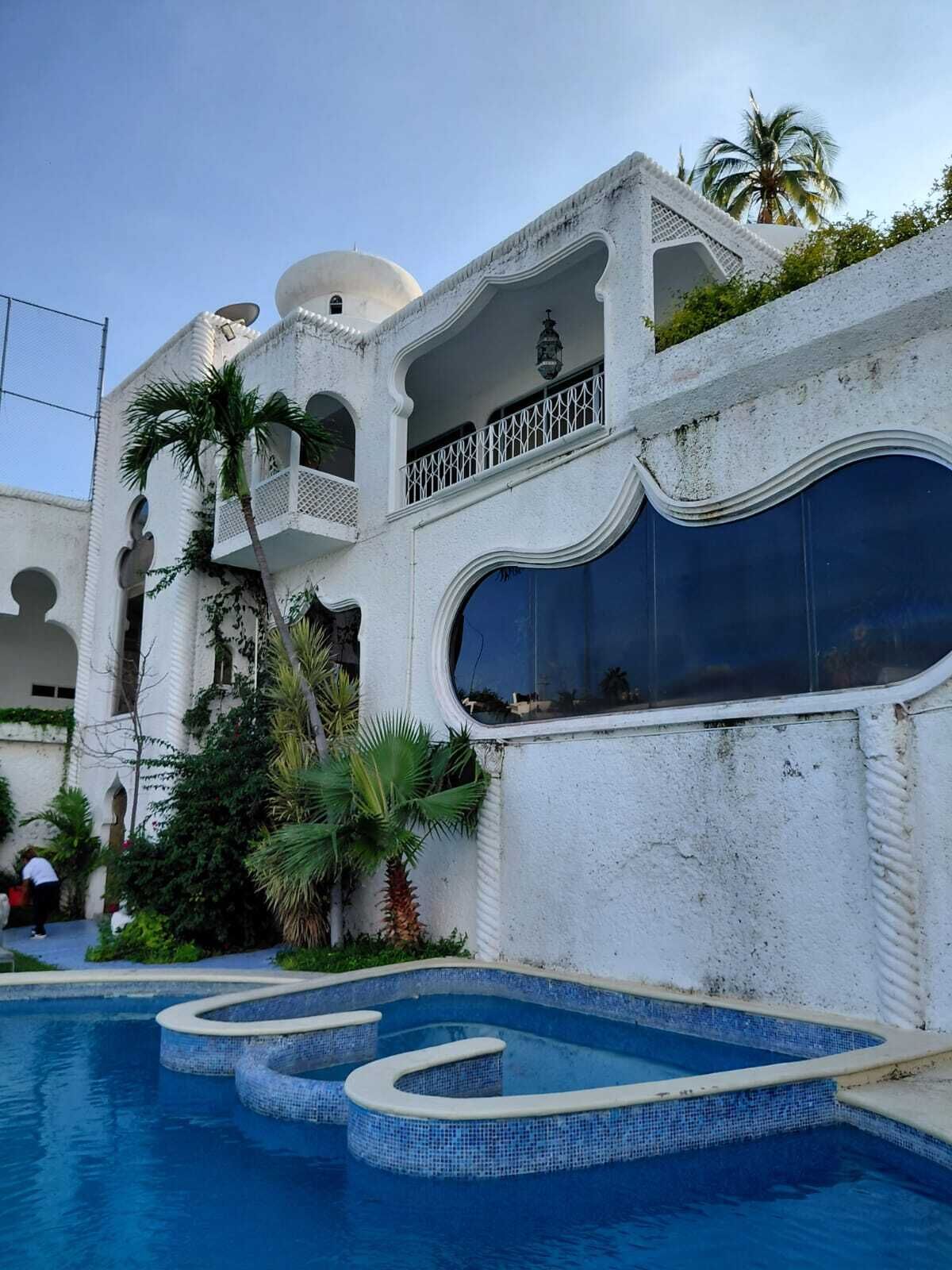 Ein weißes Gebäude mit Swimmingpool, Palmen und einem Balkon.