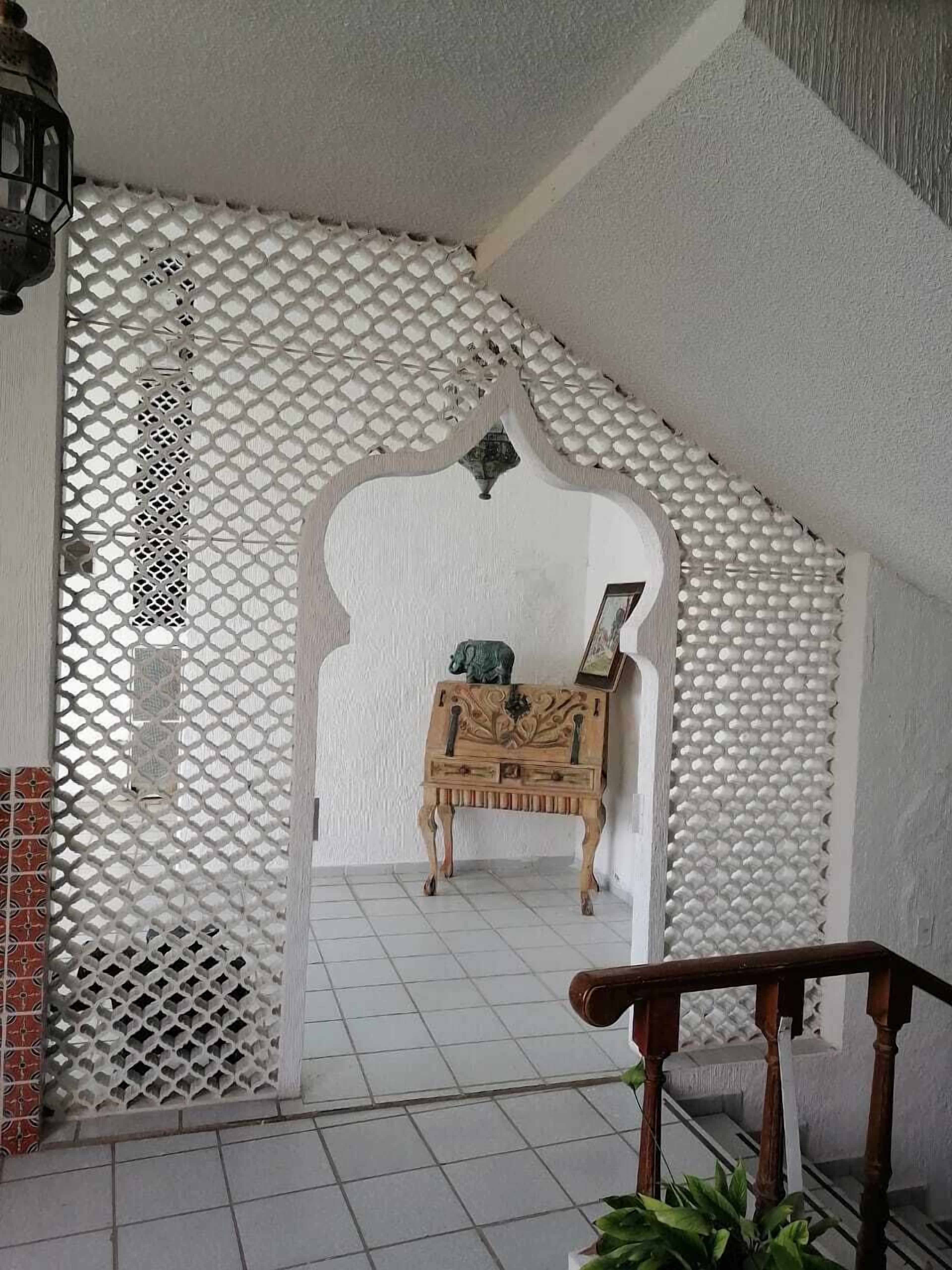 A room with a white lattice partition, a wooden cabinet with a picture frame, and a staircase with a wooden railing.