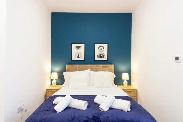 A hotel room with a bed, two bedside lamps, a headboard, and two framed pictures on the wall.