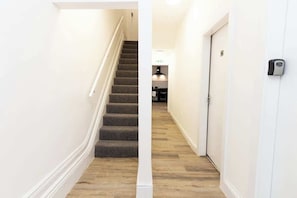 A hallway with a carpeted staircase, a door with a lock, and a light fixture on the wall.