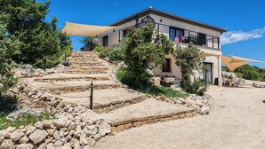 Ein modernes, zweistöckiges Haus mit einer Steintreppe, die zum Eingang führt, umgeben von Grün und blauem Himmel.