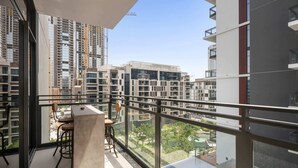 A balcony with a glass railing, a concrete table, and two chairs. - Wilton Park Res - Nad Al Sheba (Dubai)