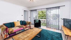 A living room with a colorful sofa, a wooden coffee table, and a view of a balcony with a table and chairs. - 3 BR Chic Home with Balcony & Free Parking! (Leeds)