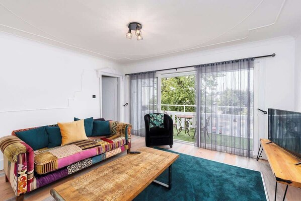 A living room with a colorful sofa, a wooden coffee table, and a view of a balcony with a table and chairs.