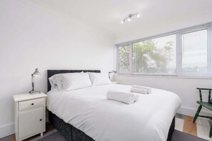 A neatly made bed with white linens, a bedside lamp, and a chair by the window.