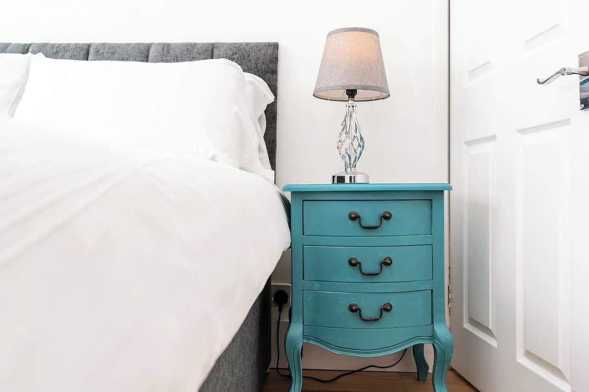 A bed with white linens, a teal bedside table with drawers, and a lamp.