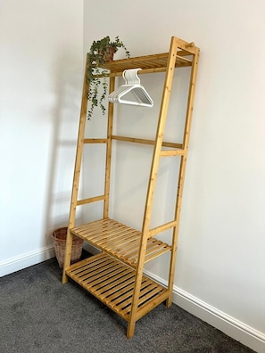 Una scaffalatura in legno con diversi ripiani e un appendiabiti, posizionata contro un muro con pavimento rivestito di tappeto.