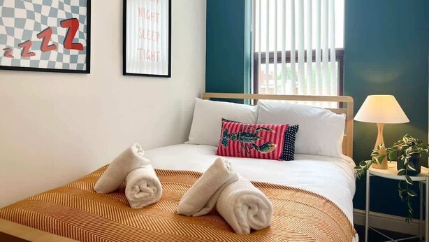 Hotelkamer met een bed, nachtkastje, lamp, raam met zonwering en twee decoratieve wandobjecten.