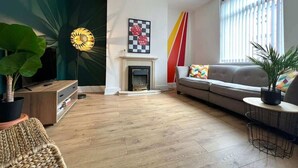 Een woonkamer met een open haard, een bank, een televisie en een grote plant.
