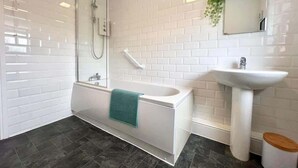 Een moderne badkamer met bad, douche en wastafel, met witte metrotegels en donkere vloertegels.