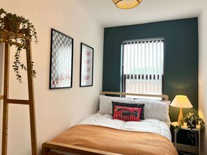 A bedroom with a bed, a window with blinds, a bedside lamp, and wall art.