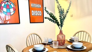 Een eetgedeelte met een ronde houten tafel, vier stoelen, een vaas met een plant en twee ingelijste foto's aan de muur.