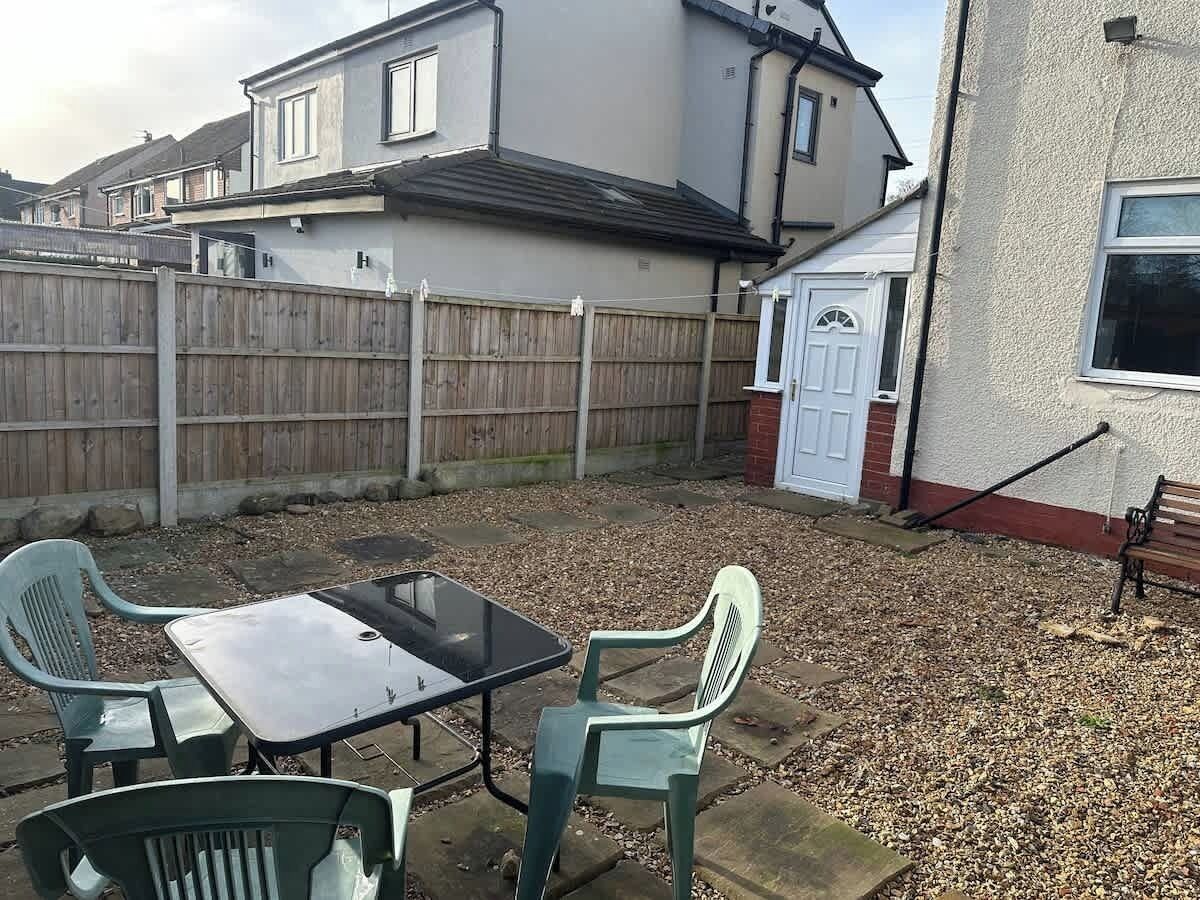 A backyard with a table and chairs, a wooden fence, and a house in the background.