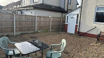 A backyard with a table and chairs, a wooden fence, and a house in the background.