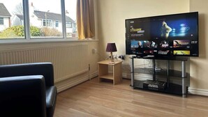 Ett vardagsrum med en tv som visar en film, en soffa, ett litet bord med en lampa och ett fönster med gardiner.