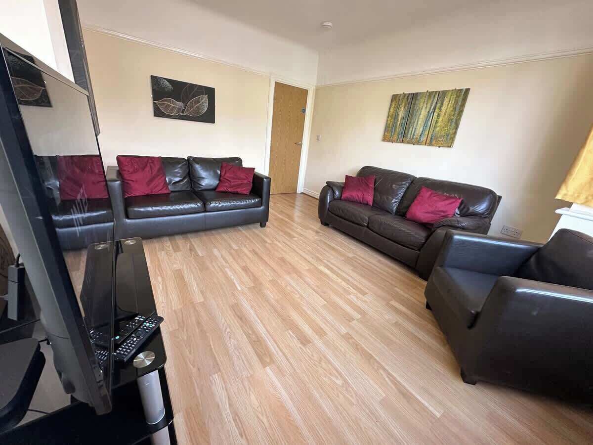 A living room with two leather sofas, a flat-screen TV, and wooden flooring.