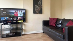 Ett vardagsrum med en platt-TV, en svart lädersoffa och ett konstverk som hänger på väggen.
