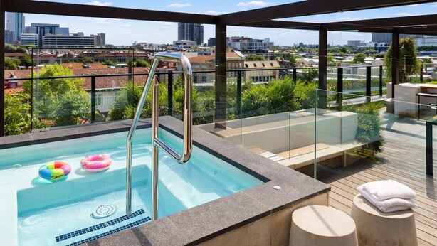 Une piscine sur le toit offrant une vue sur la ville, avec des rampes en verre et une terrasse en bois.