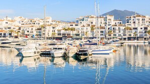A marina with numerous boats docked, surrounded by multi-story buildings with balconies and palm trees.