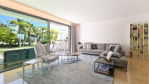 A modern living room with a large window, a grey sofa, striped armchairs, a coffee table, and a bookshelf.