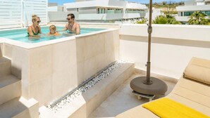 A rooftop pool area with a hot tub, lounge chairs, and an umbrella.