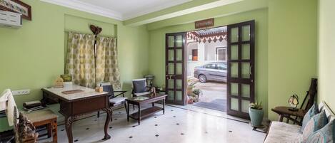 Quarto com escrivaninha, cadeira, sofá e uma janela grande com vista para um carro estacionado lá fora.