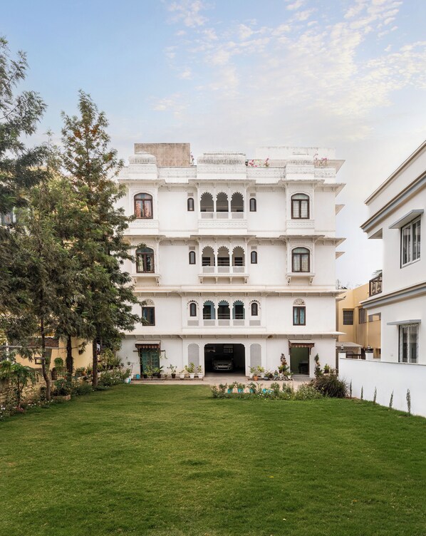A multi-story building with a central entrance, surrounded by a well-maintained lawn and trees. - Chandra Vilas Heritage stay (Udaipur)