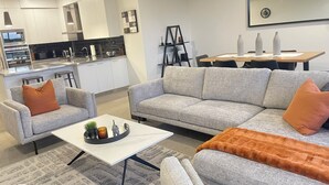 Ein modernes Wohnzimmer mit grauem Sofa, einem Couchtisch und einem Essbereich mit Tisch und Stühlen.