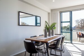 Ein zeitgemäßer Essbereich mit Holztisch, schwarzen Stühlen und einem großen Fenster mit Blick ins Freie.