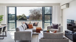 Ein modernes Wohnzimmer mit einer Eckcouch, einem Fernseher und einem Balkon mit Tisch und Stühlen.