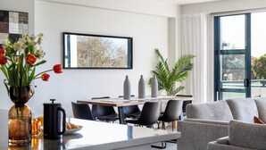Ein modernes Wohnzimmer mit einem grauen Sofa, einem Esstisch mit Stühlen, einer Kaffeemaschine und einer Vase mit Blumen.