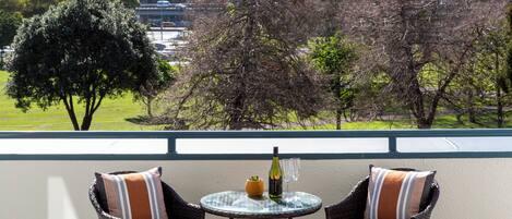 A balcony with wicker chairs and a glass table, a bottle, and two glasses.