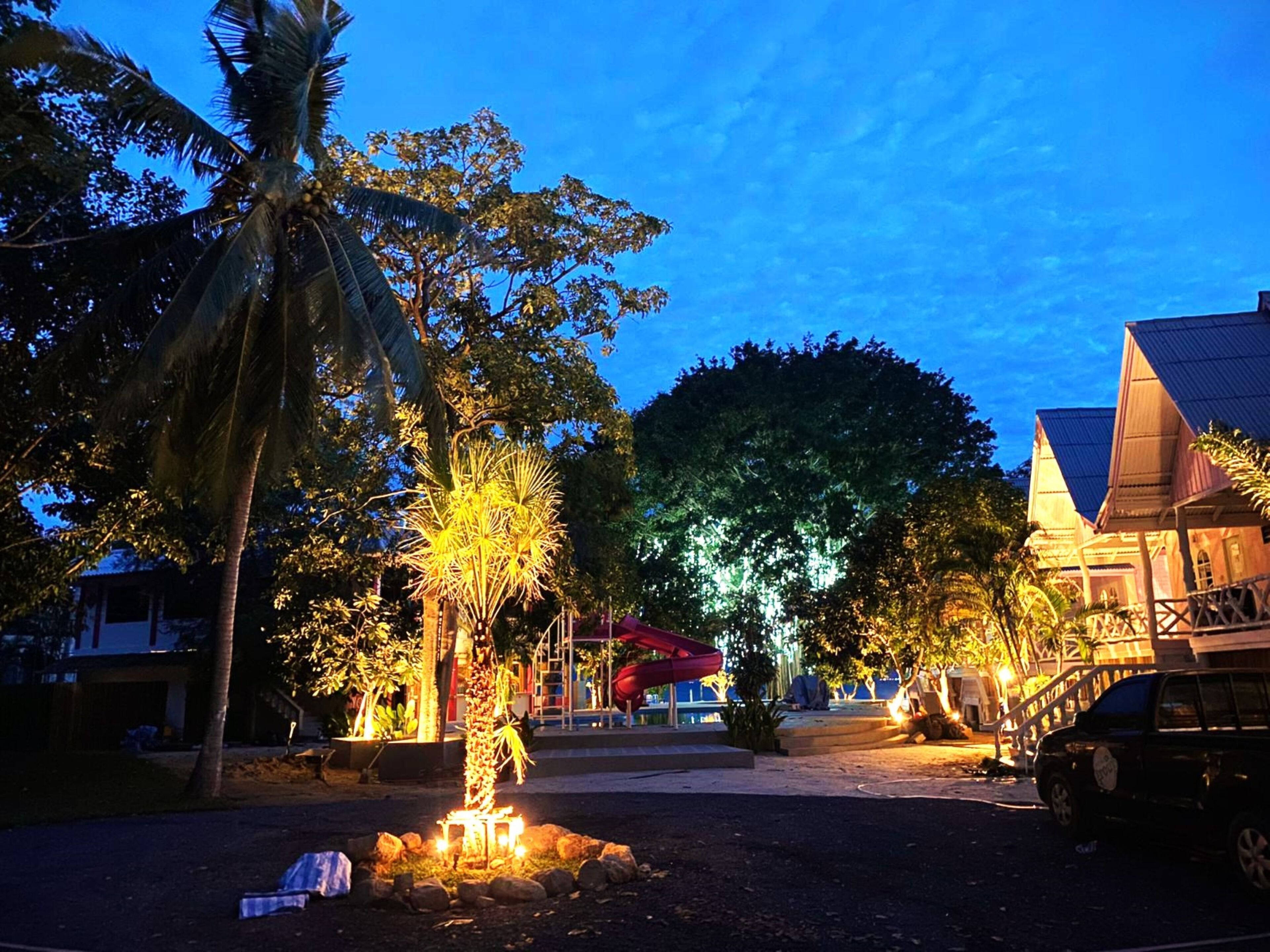 A well-lit outdoor area with palm trees, a red slide, and a building with a sloped roof.