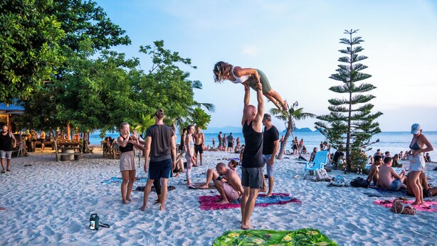 A crowded beach with people engaging in various activities, including a man lifting a woman. - Slumber Party Beach Koh Phangan (Ko Pha-ngan)
