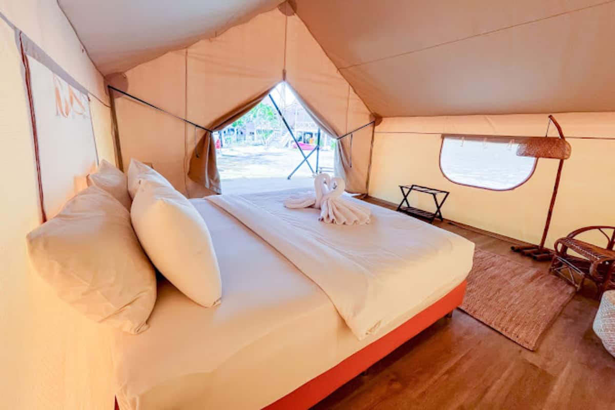 A tented room with a bed, pillows, a window, and a small table.