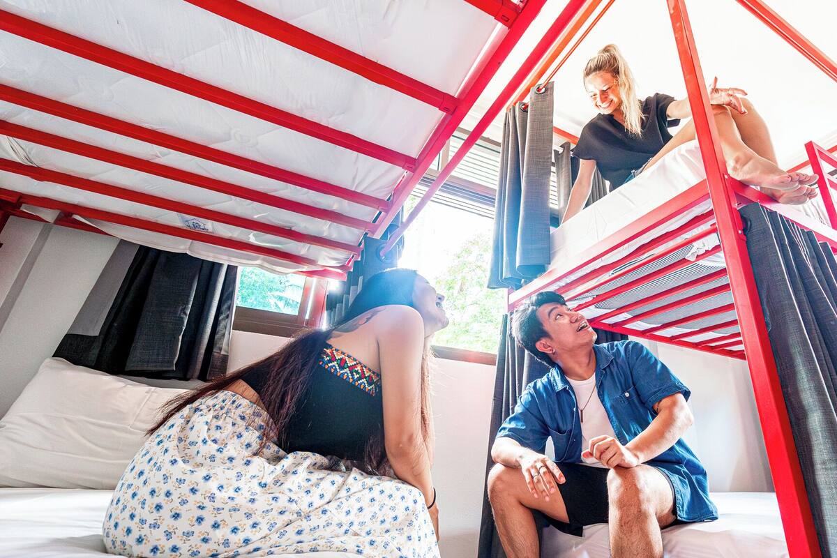 A room with a bunk bed, a window with curtains, and a bed with a floral-patterned cover.