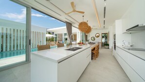 A modern kitchen with a large island, a ceiling fan, and a view of the pool. - Modern Open Design 4BR Pool Villa Mina (Rawai)