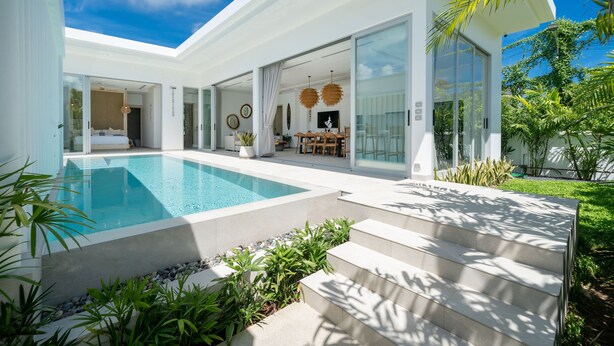 A modern house with a swimming pool, large glass doors leading to a dining area, and a well-maintained garden. - Modern Open Design 4BR Pool Villa Mina (Rawai)